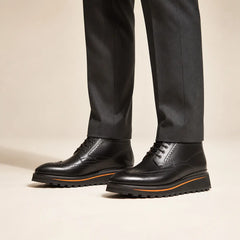 Black Brogue Chukka Boot on foot, warm off-white studio