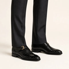 Black crocodile monk strap shoes worn with charcoal tailored trousers in a warm studio.