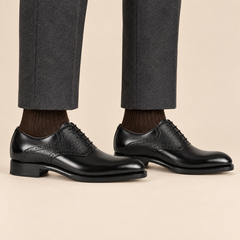 Black plain-toe Oxford shoes with textured panels worn with tailored trousers