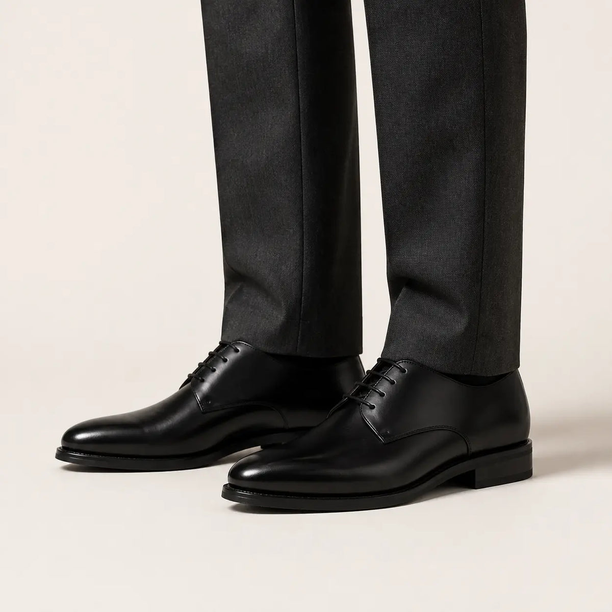 Black Plain-Toe Derby Shoe on foot, warm off-white studio