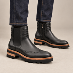 Black lug sole wingtip Chelsea ankle boots — on-foot studio view