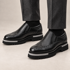 DIVINCH black glossy wingtip brogue lug-sole slip-on shoes worn with tailored charcoal trousers