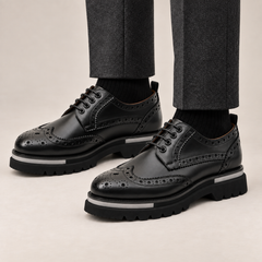 DIVINCH black glossy wingtip brogue lug-sole Derby shoes worn with tailored charcoal trousers
