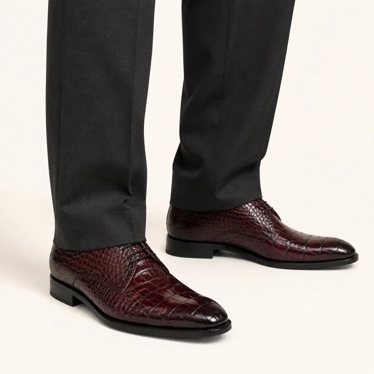 Burgundy crocodile Derby shoes worn with charcoal tailored trousers in a warm studio.