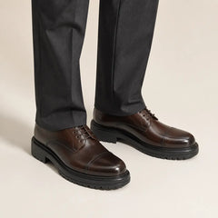 Classic Brown Cap-Toe Derby on foot, warm off-white studio