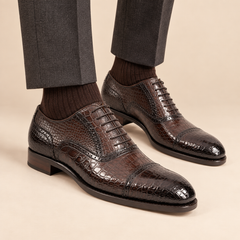Dark brown crocodile-embossed cap-toe Oxford shoes with perforated detail on model