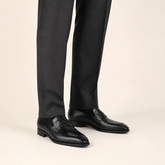 Black crocodile penny loafers worn with charcoal tailored trousers in a warm studio.