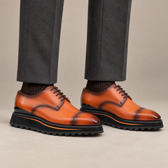 Orange-brown cap-toe Derby shoes with black lug sole on model