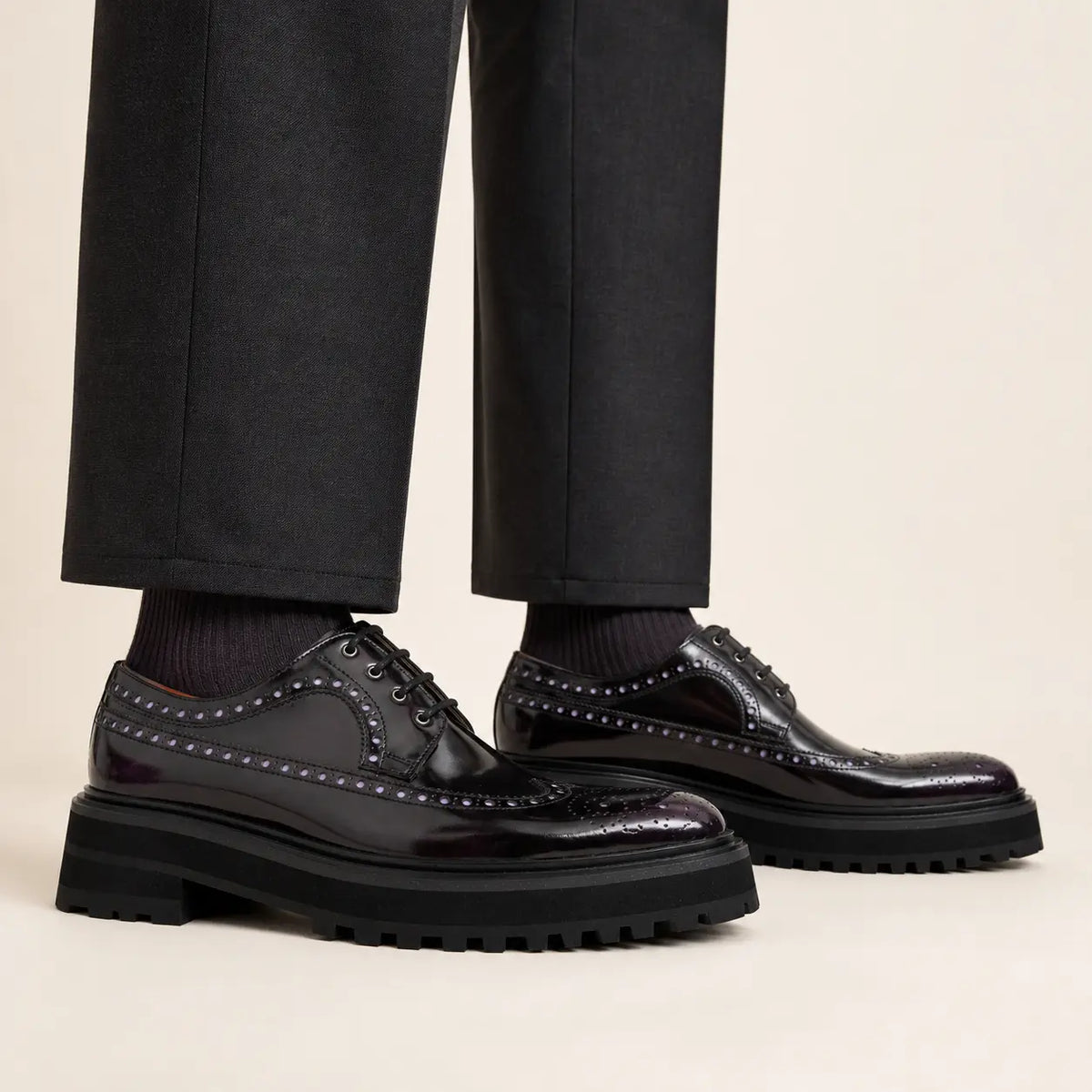Elongated polished dark plum brogue Derby shoes with black lug soles worn with relaxed straight charcoal trousers and dark socks
