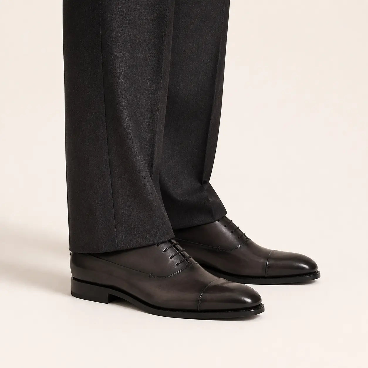 Shadow grey Oxford shoes worn with charcoal tailored trousers in a warm studio.